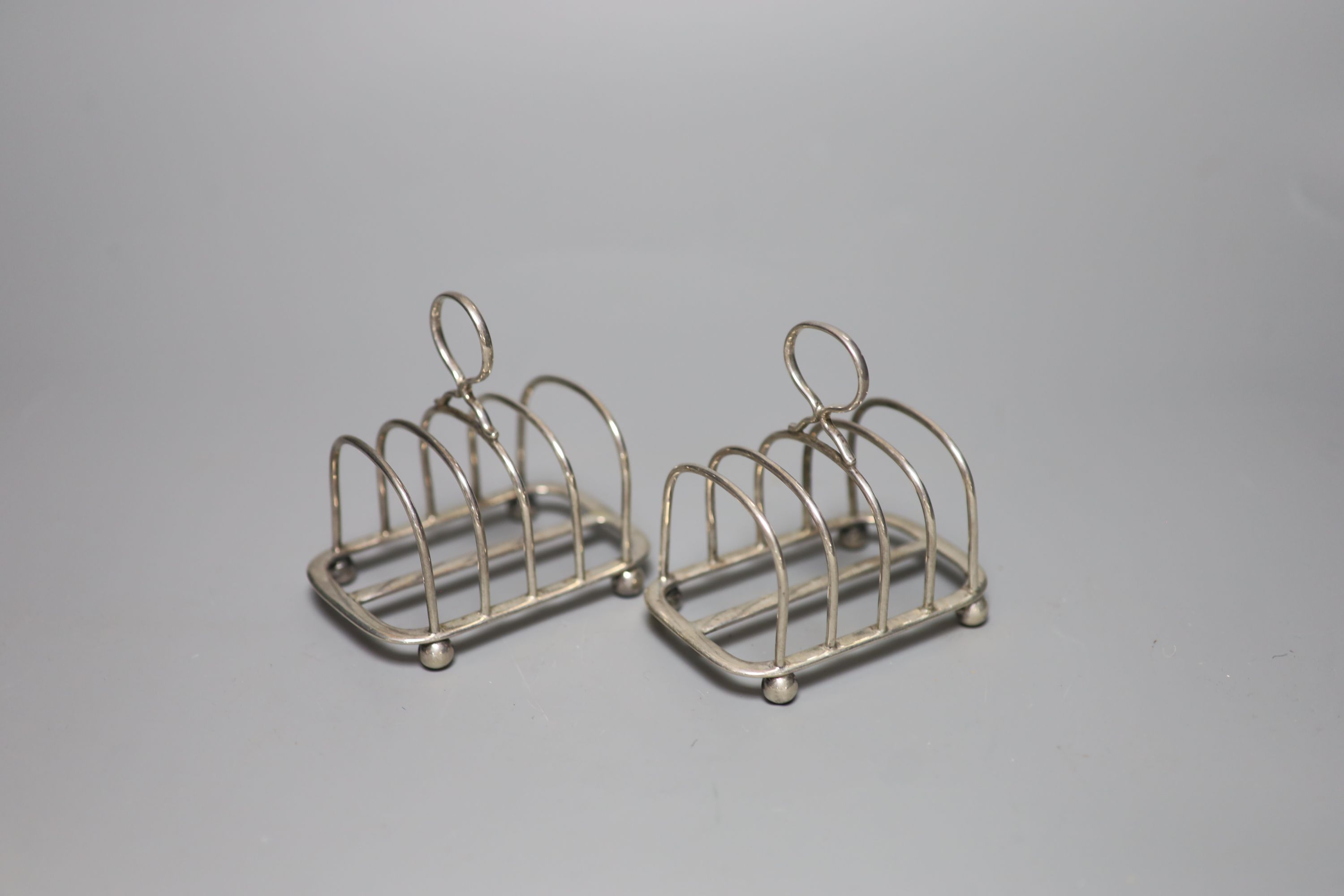 A pair of George V silver toast racks, a silver tea strainer and a silver three piece condiment set.